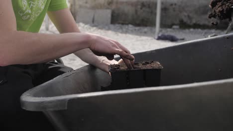 man puts soil from wheelbarrow to plastic container with bare hands, closeup