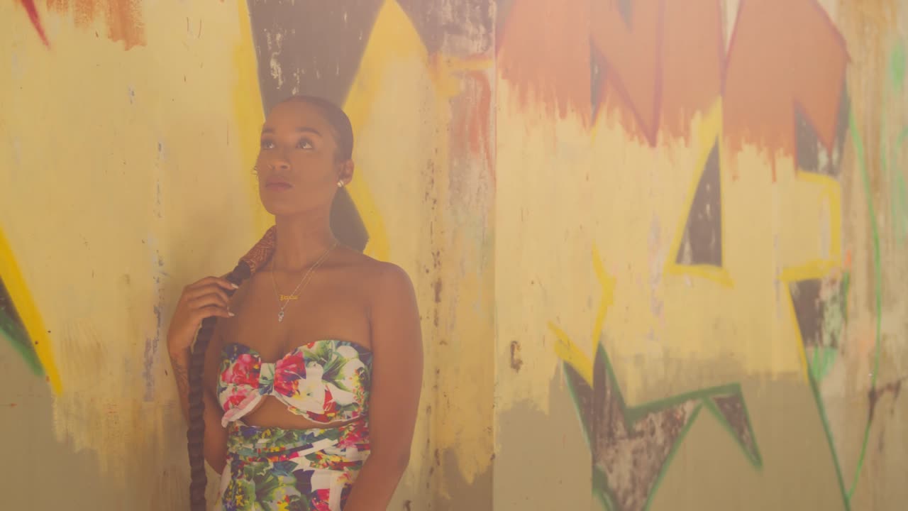 chica sexy con un vestido de flores juega con ella mientras está de pie junto a un graffiti en una pared