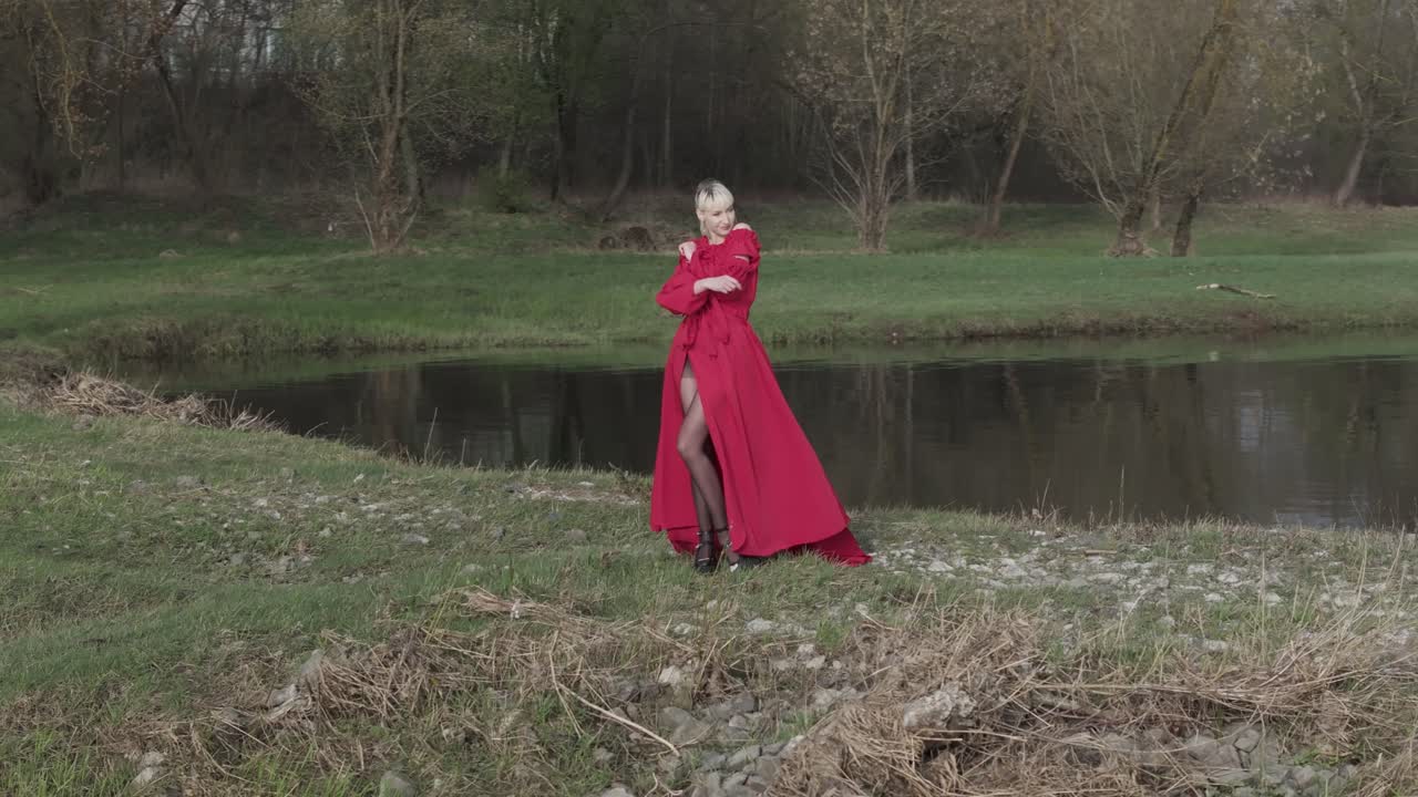 un modelo con un vestido rojo vibrante posando para una cámara en la naturaleza cerca del agua