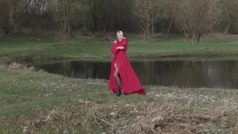 una modella con un abito rosso vibrante che posa per una telecamera in natura vicino all'acqua