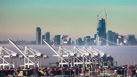 Cranes-loading-and-unloading-cargo-ships-in-the-San-Francisco-Bay---time-lapse-on-a-foggy-morning-with-the-city-skyline