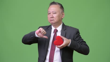 발렌타인 데이를 위해 준비된 은 심장을 들고 있는 성숙한 일본인 사업가