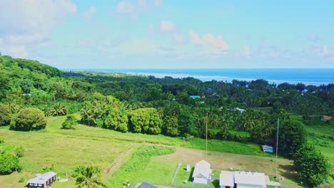 Drone-fly-over-of-rural-Rarotonga-featuring-a-solar-site,-tropical-lush-bush-with-distant-ocean-views