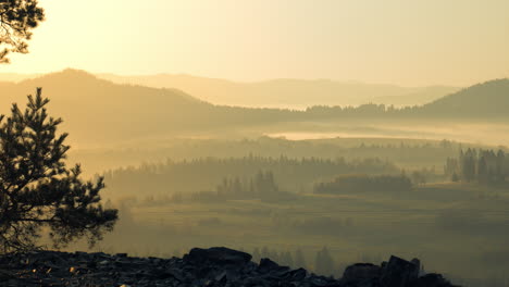 Countryside-with-hills-and-fields-covered-in-morning-mist-with-yellow-sunrise-and-orange-sky