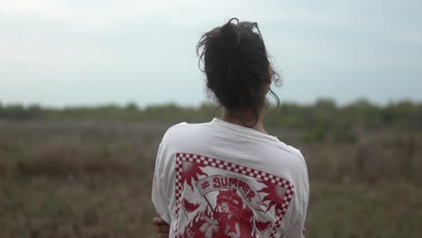 A-woman-in-a-summer-shirt-gazes-over-a-serene-grassy-field-on-an-overcast-day