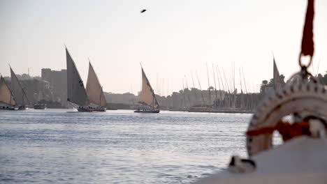 view of the front of a felucca with feluccas sailing in the backgroudn during golden hour on the nile river, aswan, egypt