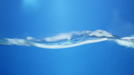 Waves-of-crystal-clear-blue-waters-bursting-and-splashing,-creating-tiny-bubbles-and-droplets