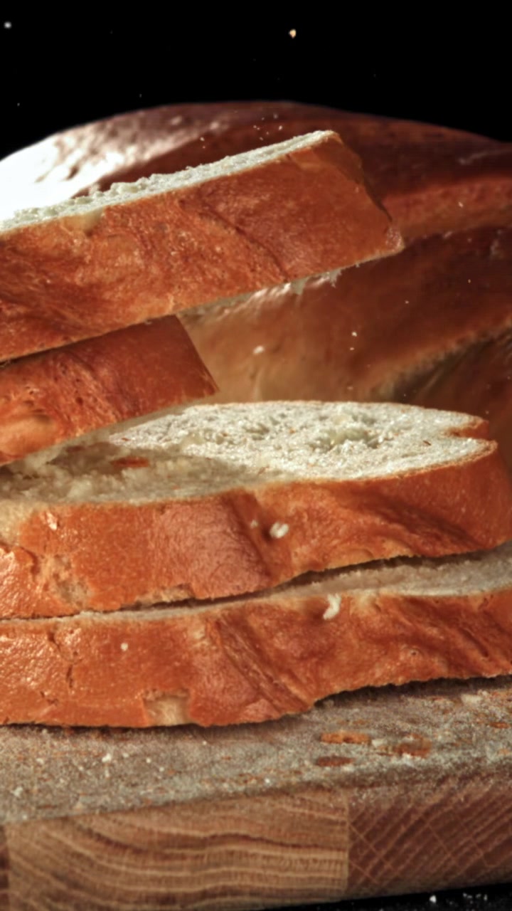 Pane appena affettato che cade al rallentatore su un tagliere di legno