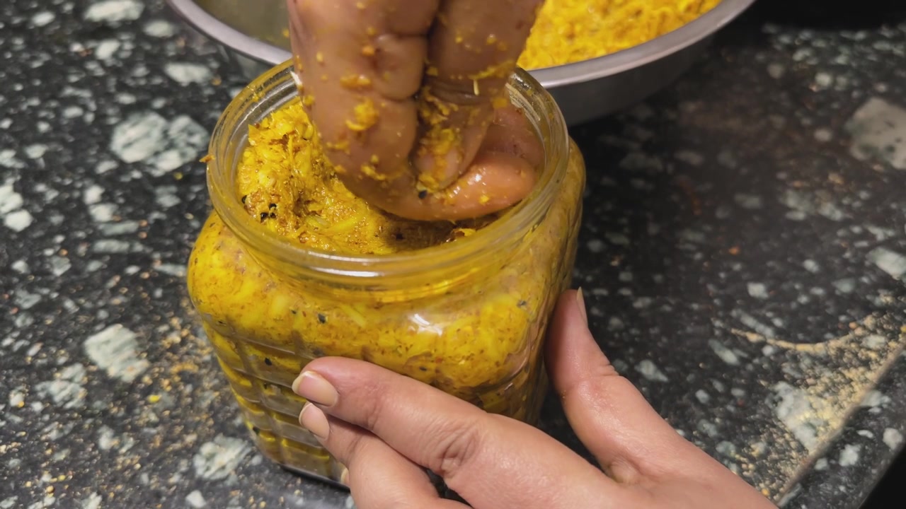 Geleneksel Hint acar saklama işlemi sırasında hava boşluklarını gidermek ve korumayı iyileştirmek amacıyla taze hazırlanmış mango turşusunu cam bir kavanozun içine dikkatlice bastıran ellerin yakın çekimi.