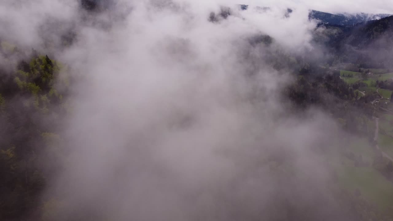 Drone slow fly through clouds over a moody forest mountain valley during spring time
