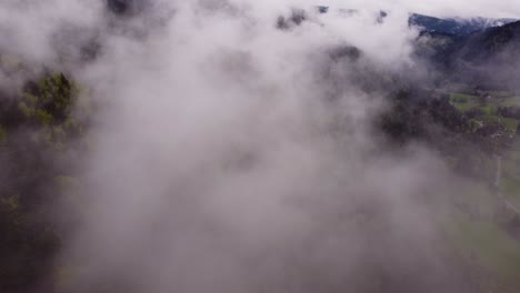 drone slow fly through clouds over a moody forest mountain valley during spring time