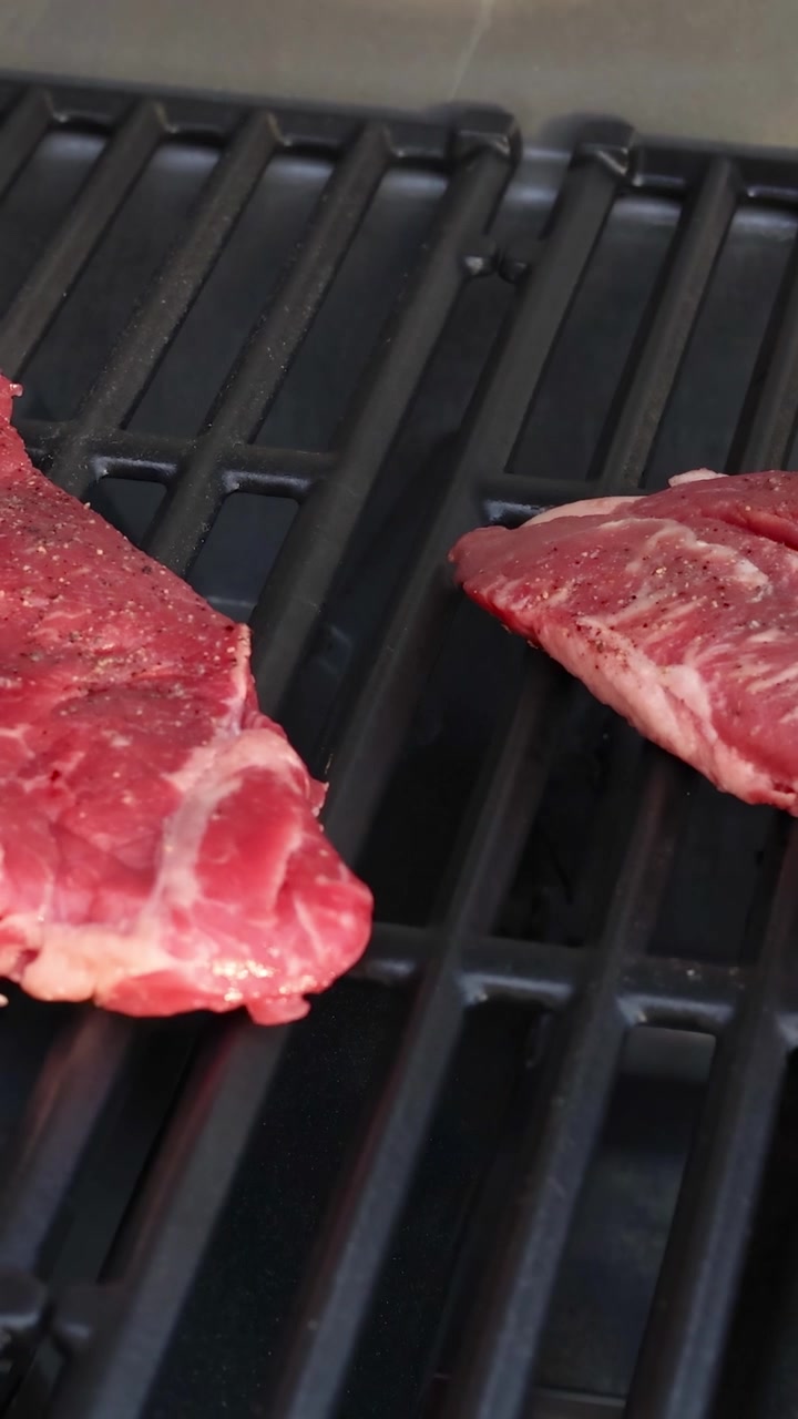 Raw beef steak placed on a barbecue grill, beginning to cook. Outdoor setting with natural lighting and close-up focus