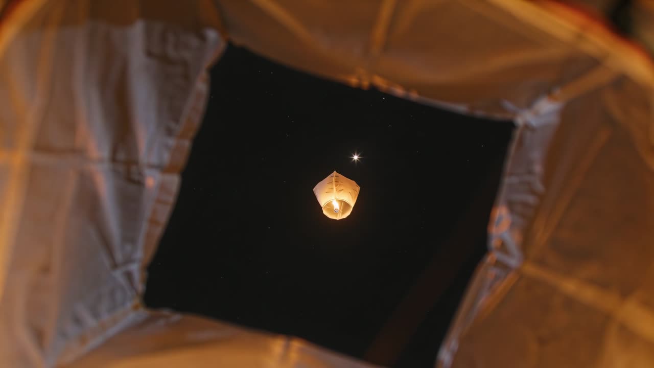 Video verticale: Lanterna di carta che si alza, la fiamma si accende attraverso l'apertura di una tenda drappeggiata di notte, con una stella sopra.