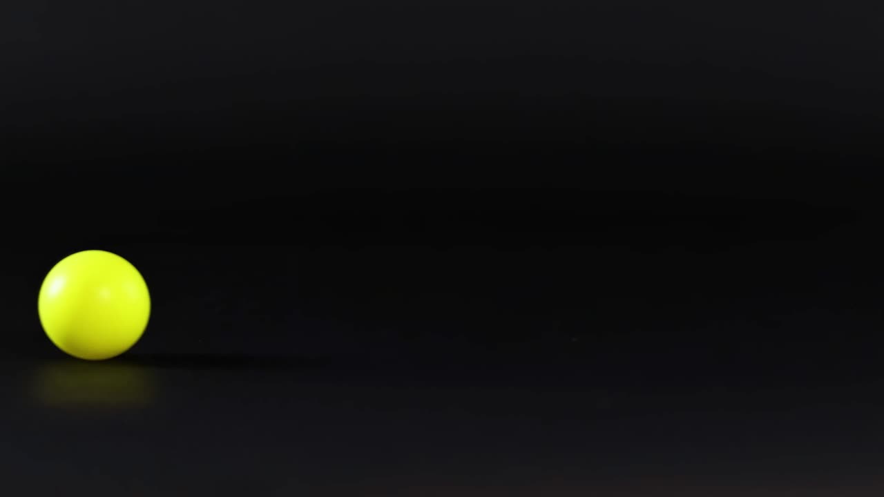 A yellow ball rolls across a smooth, dark surface in various positions.