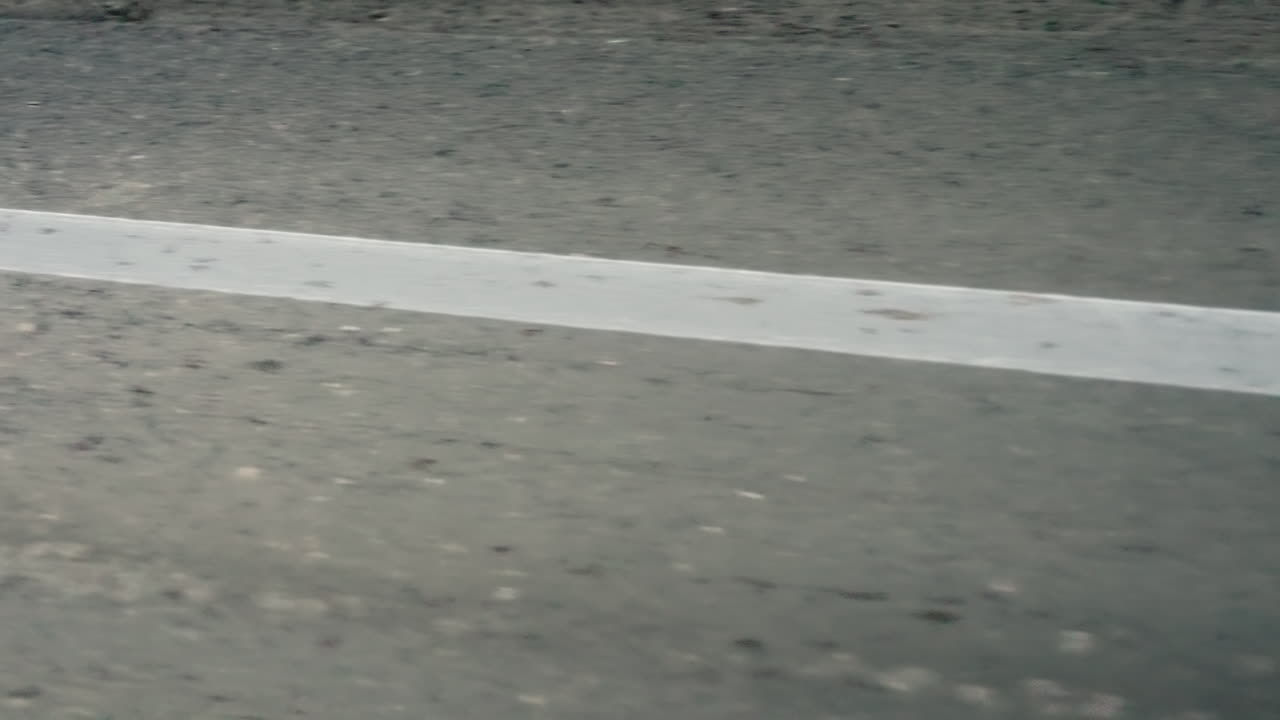 Dynamic closeup motion view of asphalt road surface with white marking line and roadside greenery, capturing speed, travel, transportation, and movement perspective