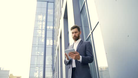 stylish bearded businessman in formal business suit standing working with tablet in hands