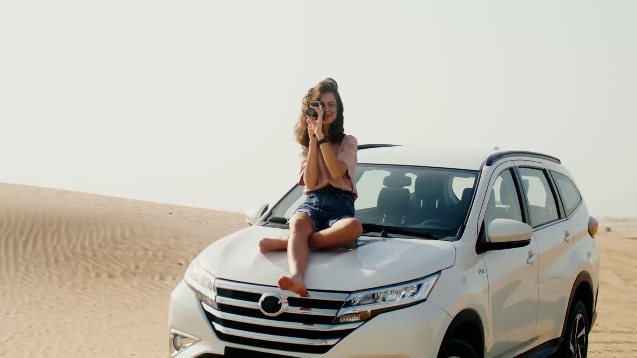 mujer tomando fotos en la parte superior de un coche en el desierto