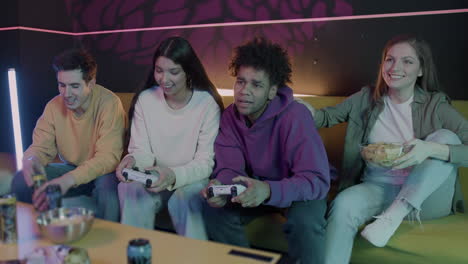 group of friends playing video games sitting on sofa at home