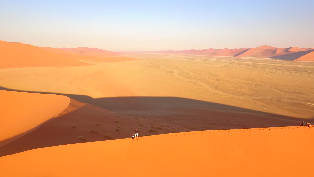 se ve a un turista en la cima de una duna de arena en namibia, áfrica meridional