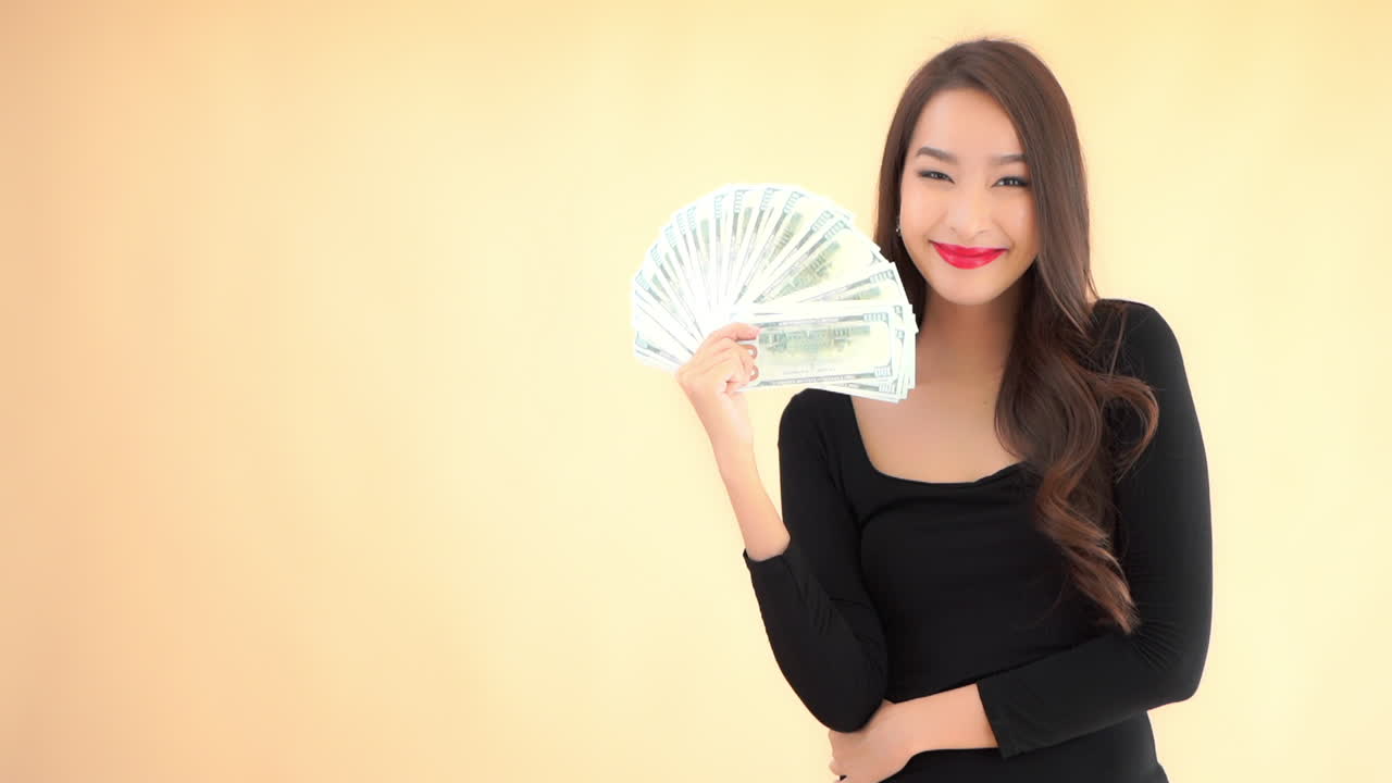 Young rich asian female showing folding fan of dollar bills cash money, like lottery winner, full frame slow motion