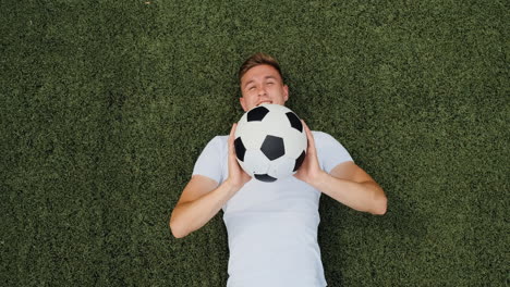 Draufsicht-Eines-Glücklichen-Jungen-Fußballspielers,-Der-Während-Der-Trainingseinheit-1-Auf-Dem-Spielfeld-Liegt,-Ball-Wirft-Und-Fängt