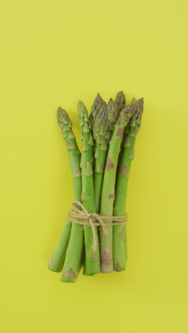 vertical video of fresh stalks of asparagus tied with rustic string on yellow background