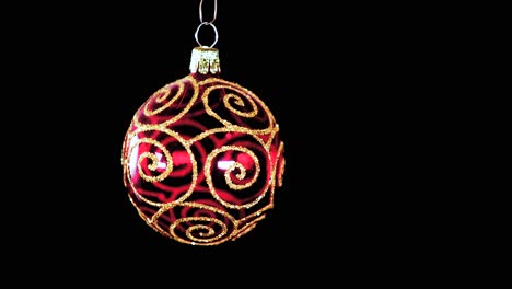 single red clear christmas ball ornament with golden glitter stripes and black background, close up