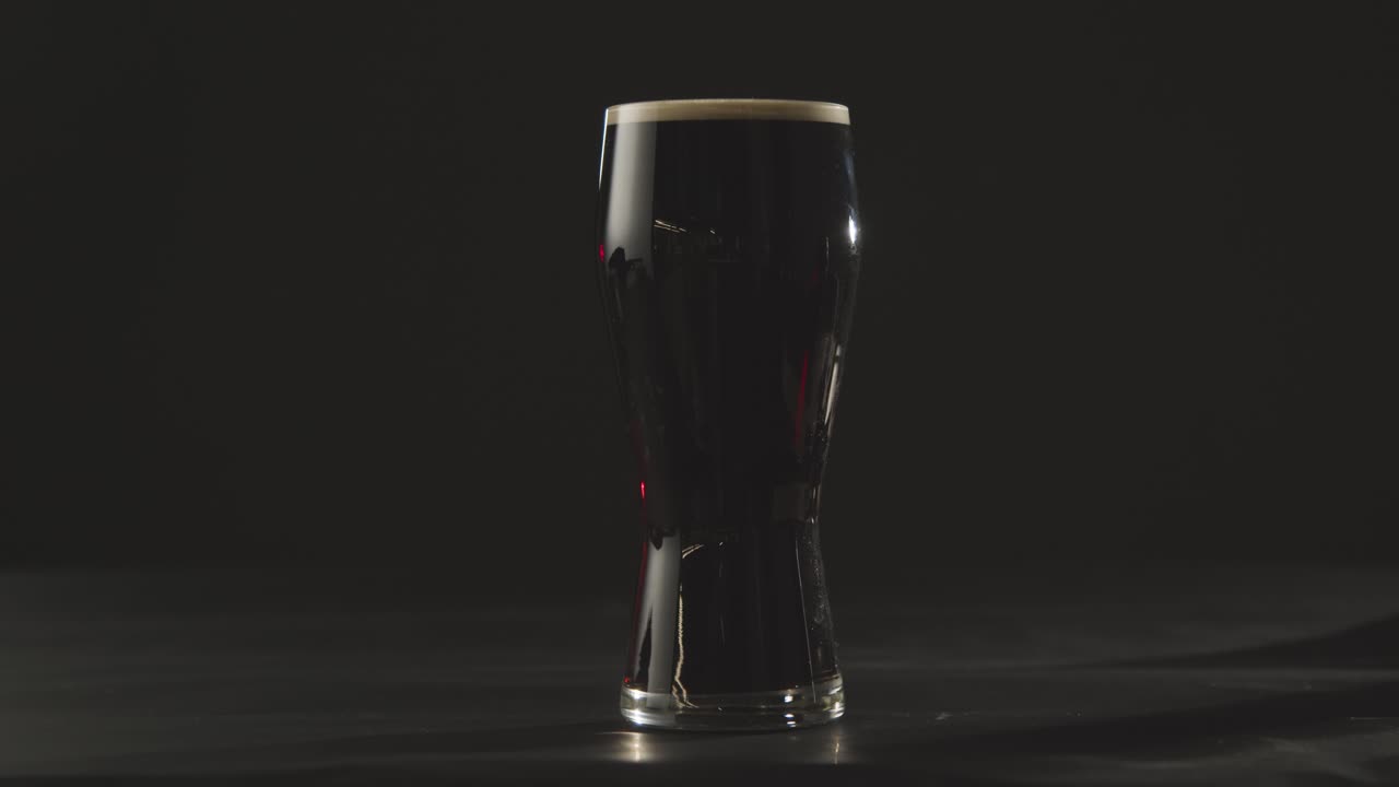 성 패트릭의 날 2를 축하하기 위해 블랙 스튜디오 배경에 유리에 아일랜드 스타우트 파인트를 집어드는 사람