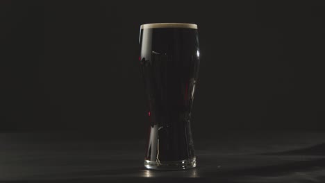 persona recogiendo una pinta de cerveza negra irlandesa en vidrio contra el fondo negro del estudio para celebrar el día de san patricio 2