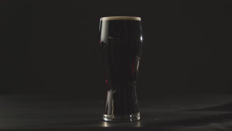 person picking up pint of irish stout in glass against black studio background to celebrate st patricks day 2