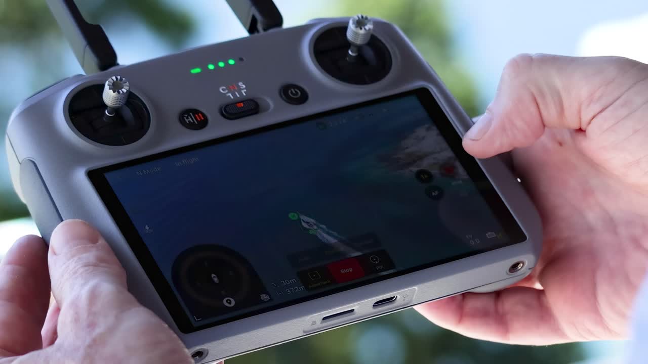Close-up of hands maneuvering a drone controller, focusing on the screen and controls.