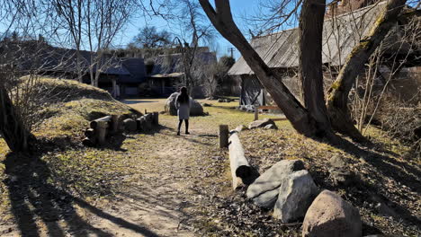 woman walking towards the old wooden buildings at open-air museum