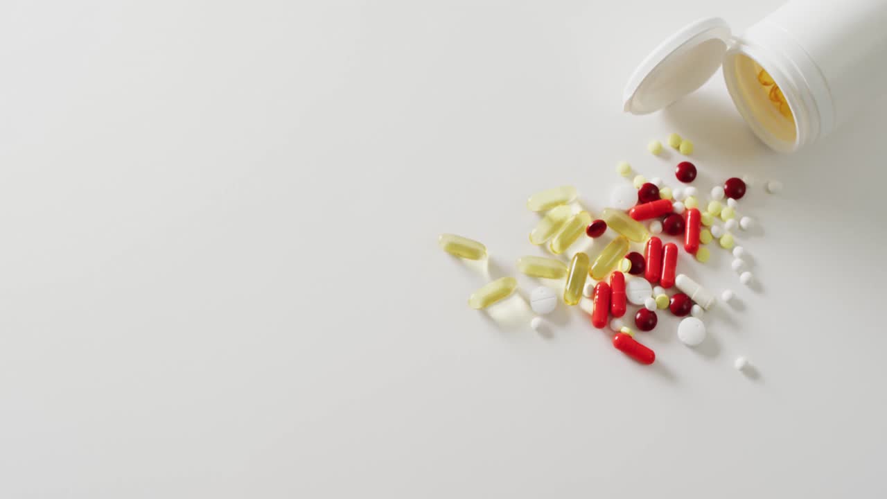 video de una caja blanca de pastillas derramando una variedad de pastillas y cápsulas sobre un fondo blanco con espacio para copiar.