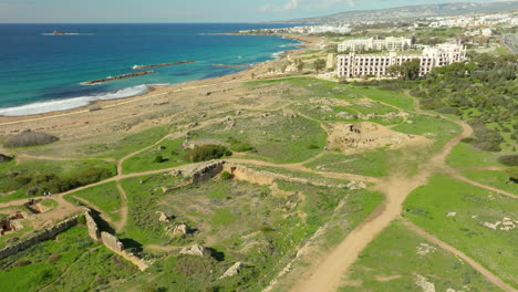 una vista aérea de las tumbas de los reyes en paphos, chipre, que muestra ruinas antiguas en el fondo del mar mediterráneo, con edificios modernos en las cercanías