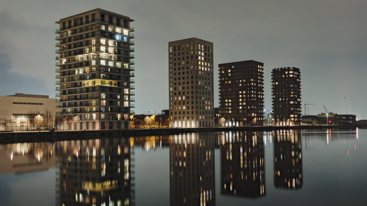 Timelapse of illuminated waterfront residential buildings in Eilandje, Antwerp, reflecting on the still water at night