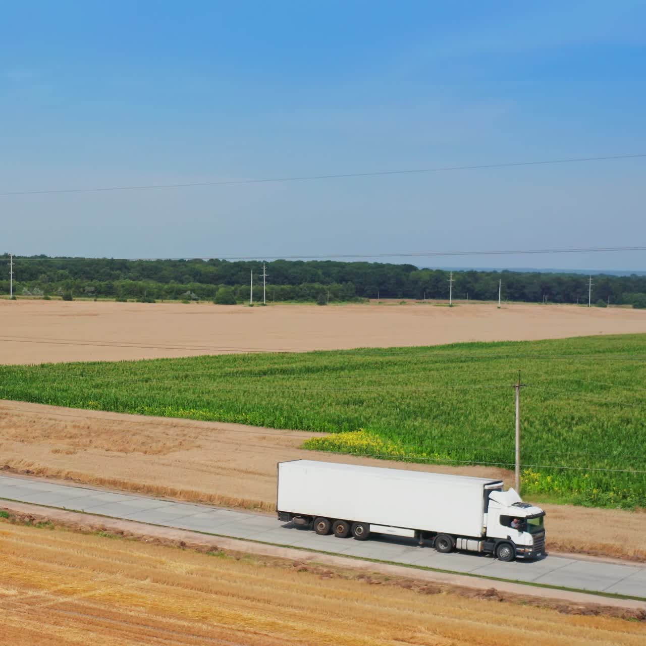 White truck going by the road crossing the farmlands. Agricultural machinery working in the field on harvest season. Top view