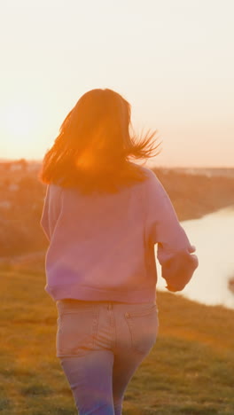 woman runs along empty riverbank at sunset light. sportive lady in jeans jogs at country riverside against evening sunlight. active leisure and hobby