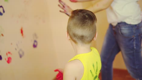 Cute-boy-showing-his-hands-in-paint.-Happy-little-child-making-colorful-handsprint-on-the-wall-with-mother-together.