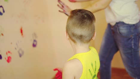 cute boy showing his hands in paint. happy little child making colorful handsprint on the wall with mother together.