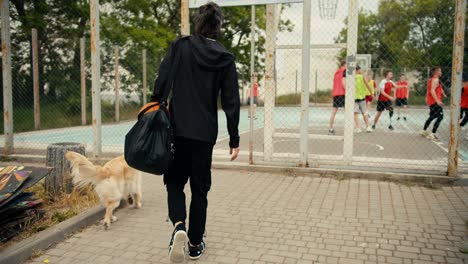 a brunette man in black clothes with a black backpack and a basketball came to the basketball game, he is the coach of the team