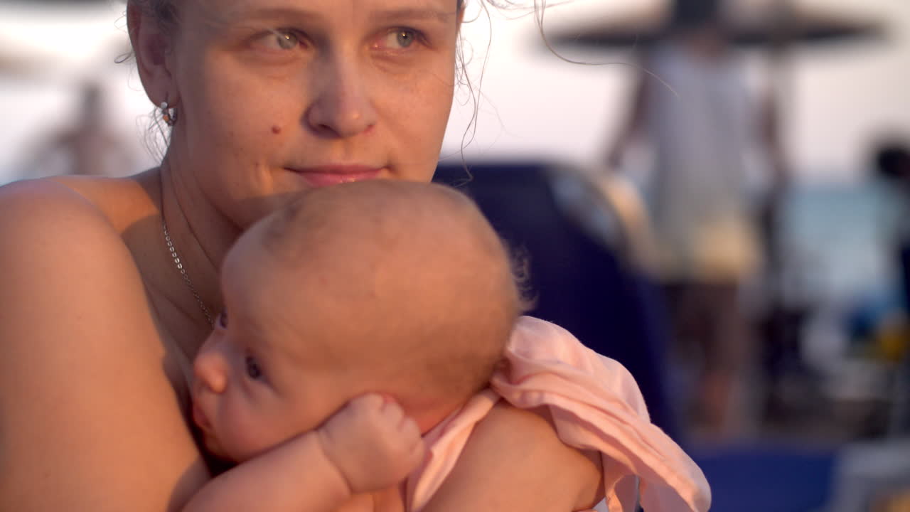 Nachdenkliche Mutter mit Baby am Strand bei Sonnenuntergang.