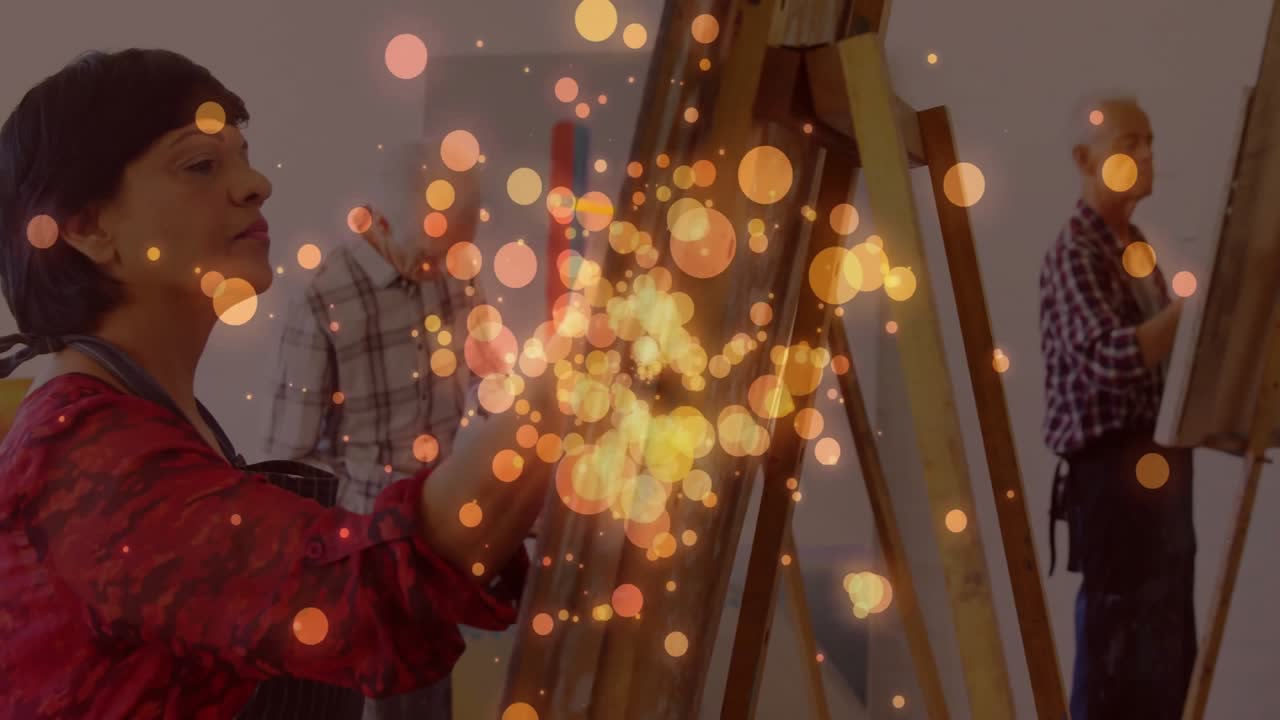 Artistas pintando enquanto a câmera percorre o estúdio de arte, misturando tintas, aplicando camadas e adicionando pinceladas em meio ao efeito bokeh.