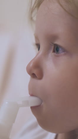 pretty little girl with blue eyes coughs using modern inhaler on blurred background extreme close view
