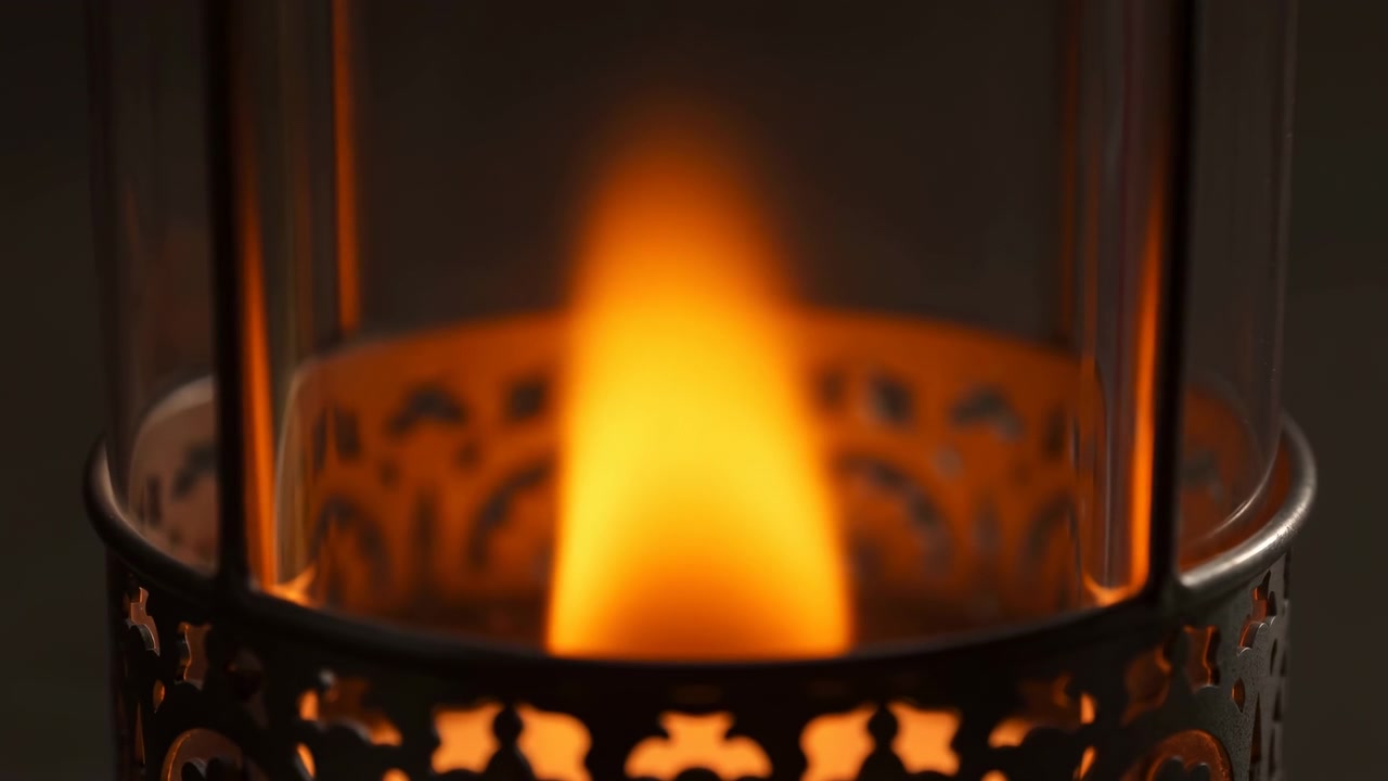 Främre närbild av tänd ljuslåga inuti en perforerad dekorativ metalllykta med en klar glasylinder, som visar synlig förändring när lågan vidgas, ljusnar och sprider mjukt varmt ljus genom lyktan.