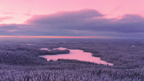aerial drone video of vast snow covered forest and an icy lake by golden hour just before sunrise