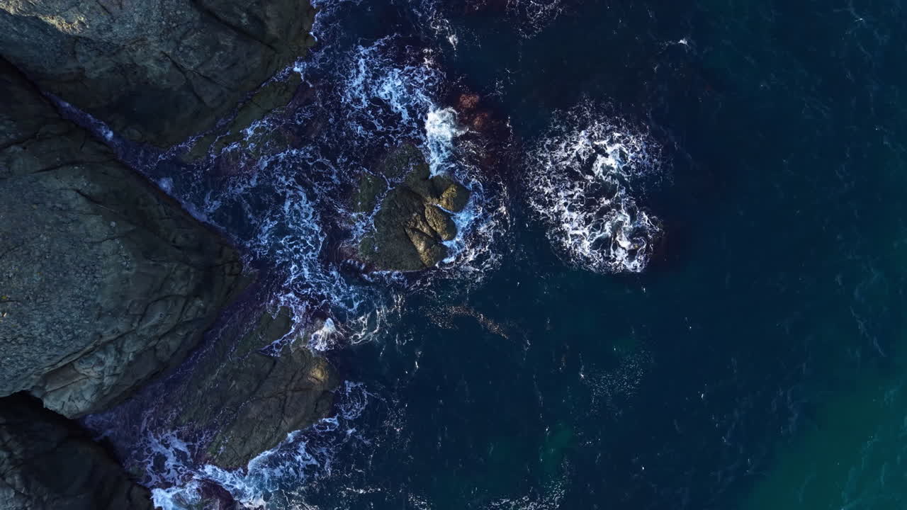 Majestic ocean waves crash against the rugged cliffs, creating a breathtaking dance of nature at sunset