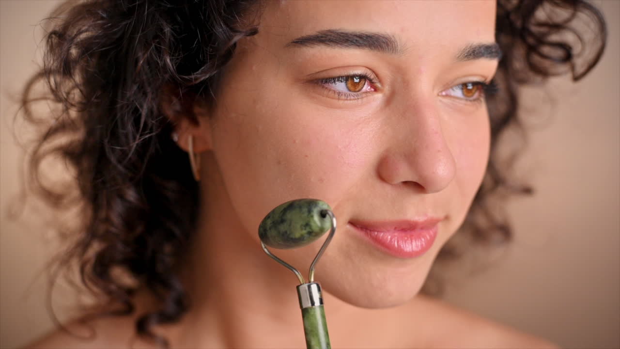 A young caucasian smiling woman is doing a facial massage using a roller. Slow motion