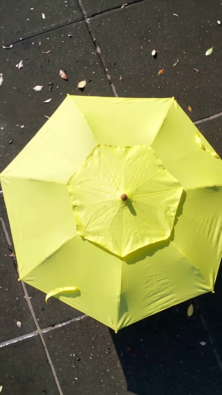 Video verticale: Telecamera che si allontana rivelando un ombrello giallo sul marciapiede per mostrare ombra e pozzanghera.