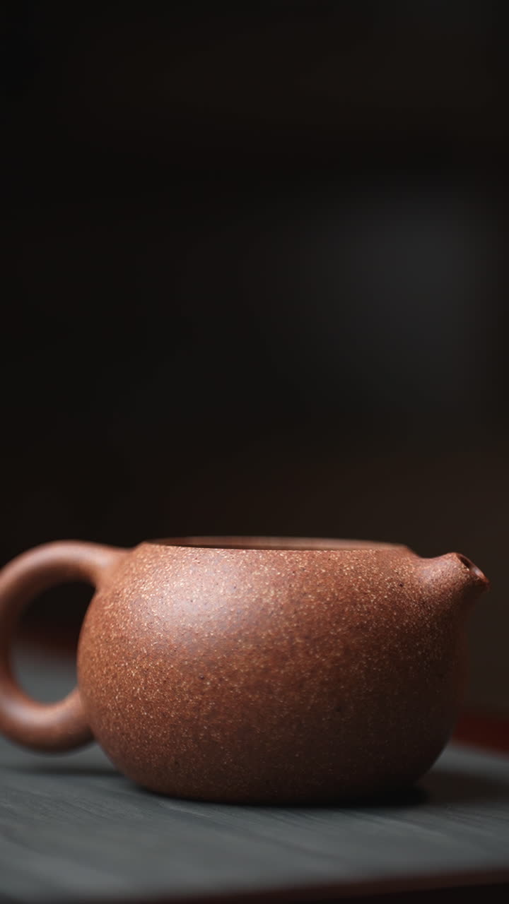 Woman's hand placing lid on small brown ceramic teapot