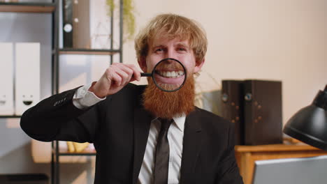 Happy-business-man-holding-magnifier-glass-on-teeth,-looking-at-camera,-smiling-silly-face-mouth